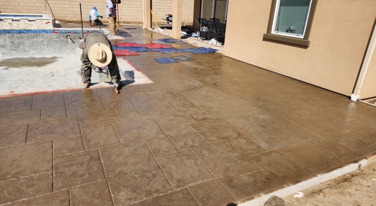 Concrete stamping underway around a pool beside a home