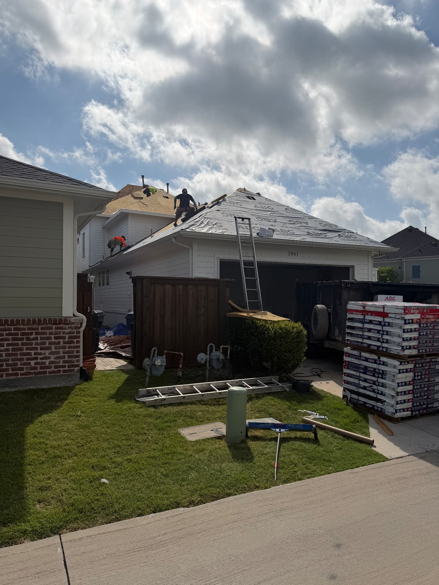 Side-yard view of roof replacement with exposed decking and roofing materials