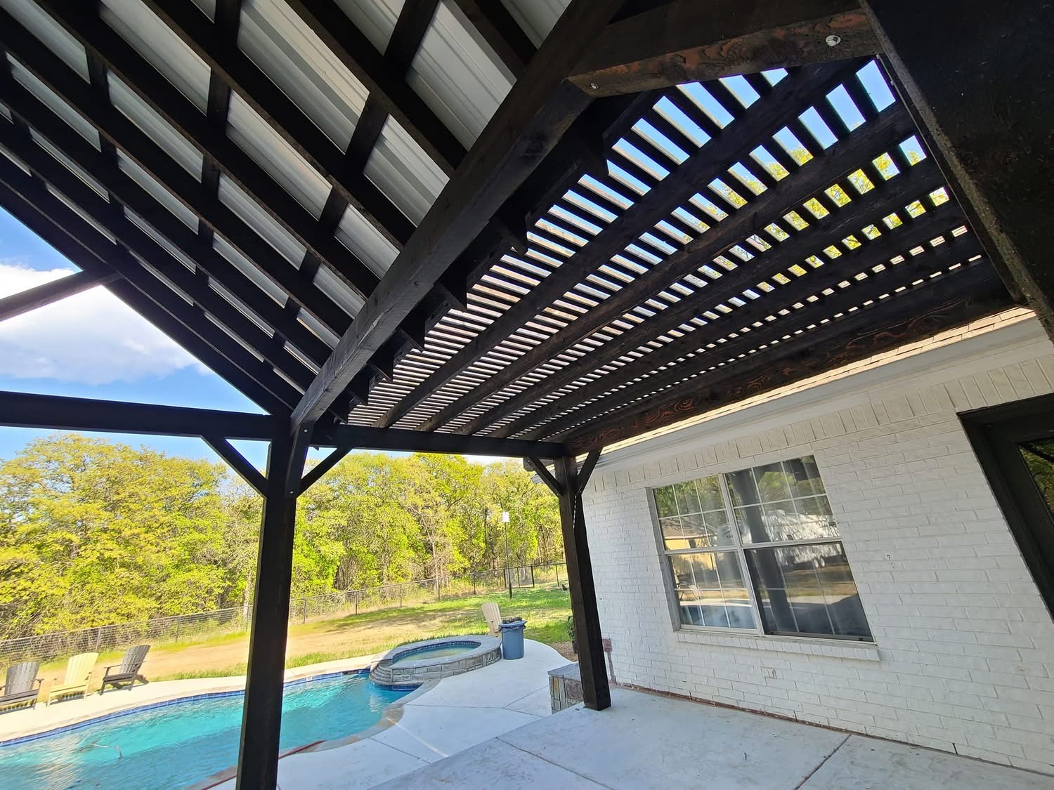 View from beneath a patio cover showing dark timber rafters and a ceiling fan