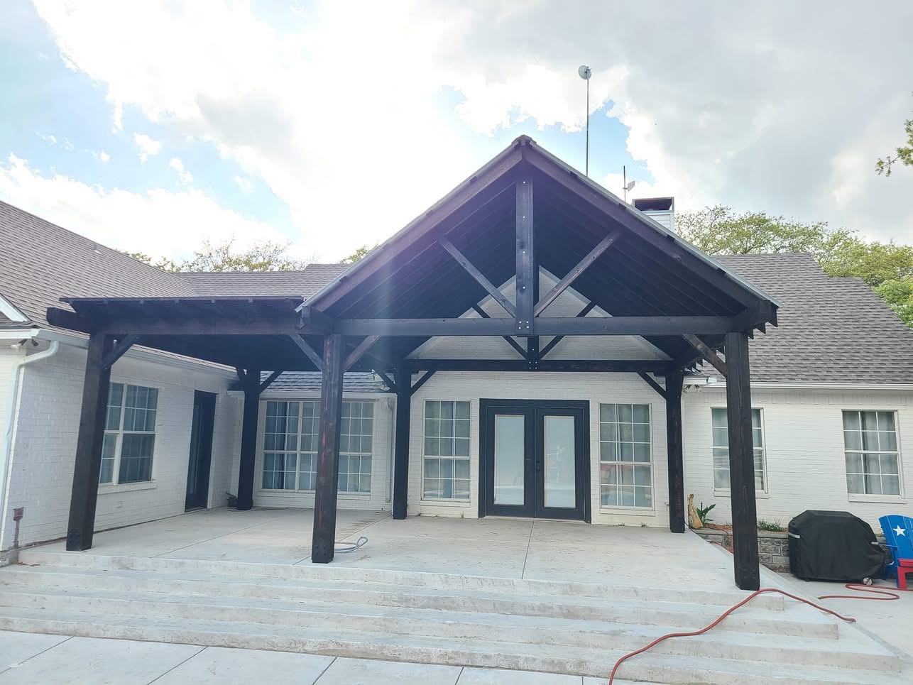 Gable patio cover with dark timber posts and a metal roof above a concrete patio