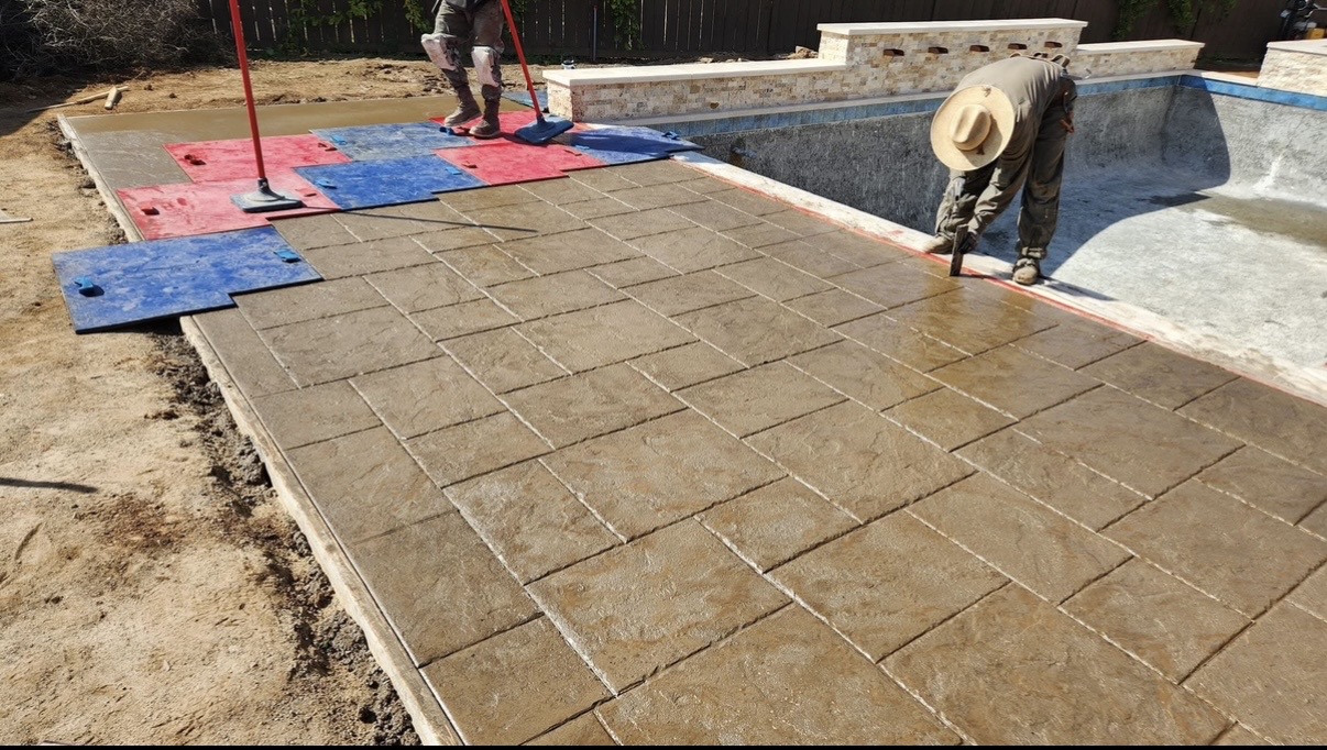 Crew stamping concrete beside a pool using colored stamping mats